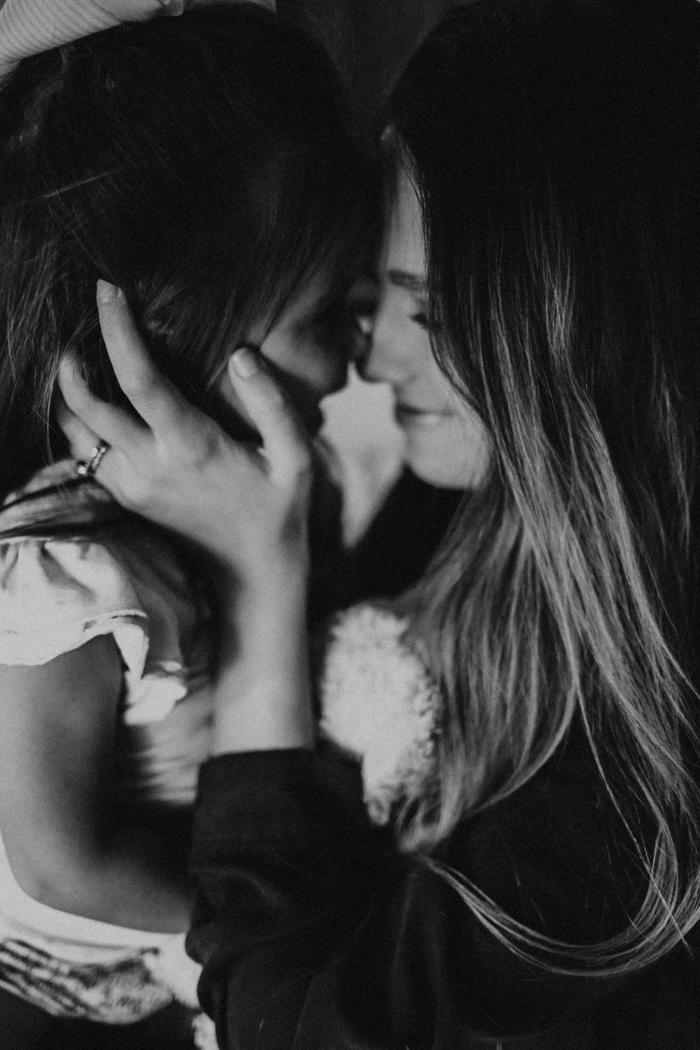 Romantic black and white photo of two women sharing an intimate moment, nearly kissing in soft light.