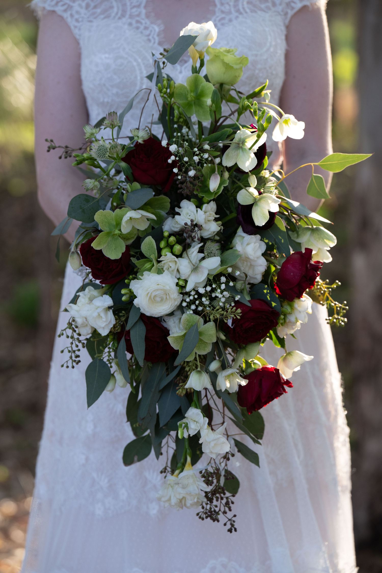 A cascading bridal bouquet with white and burgundy flowers against a lace wedding dress.
