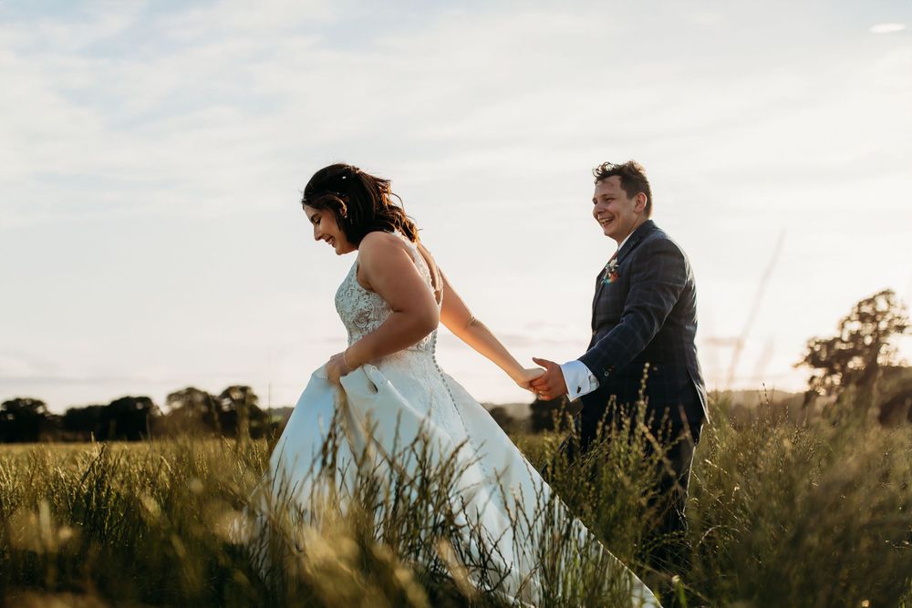 Newlyweds walk through tall grass field during golden hour photography session.