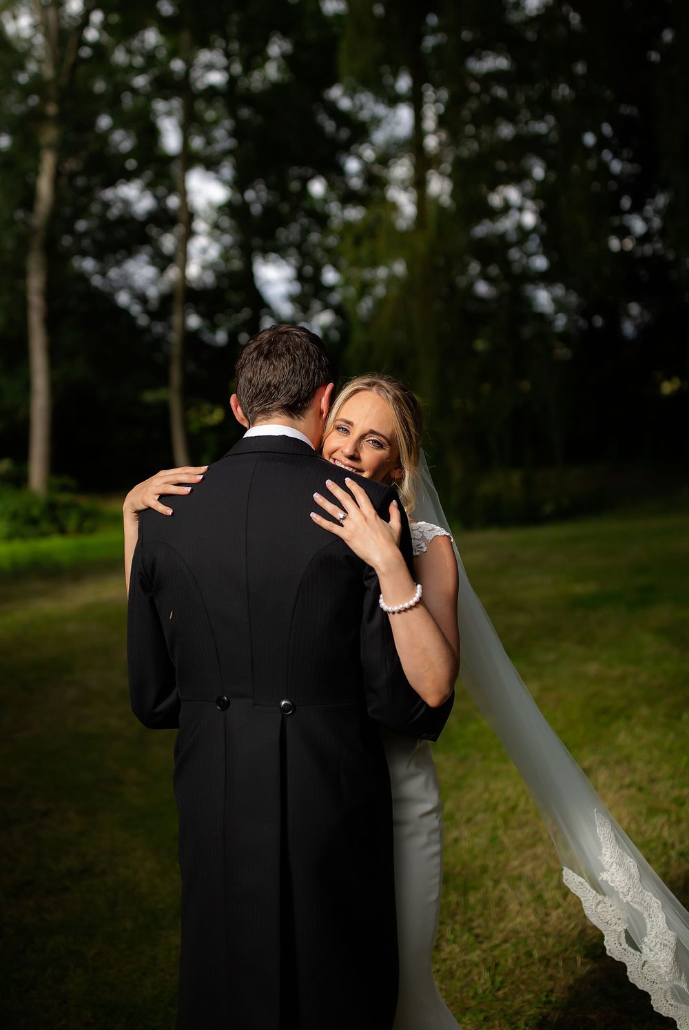 Romantic wedding couple embraces outdoors with lush greenery in background during golden hour.