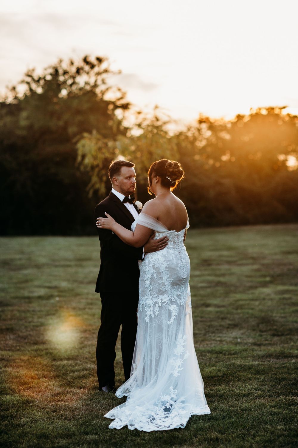Sunset wedding portrait featuring couple in elegant attire with dramatic lighting and lace dress details.