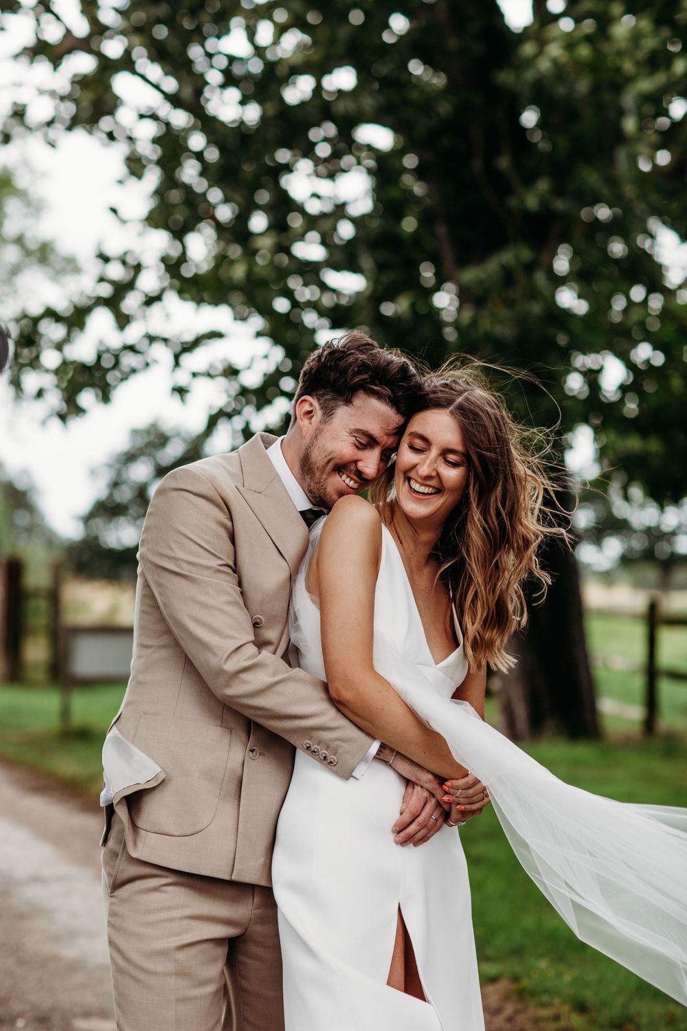 Joyful couple laughs together in casual wedding moment on garden path.