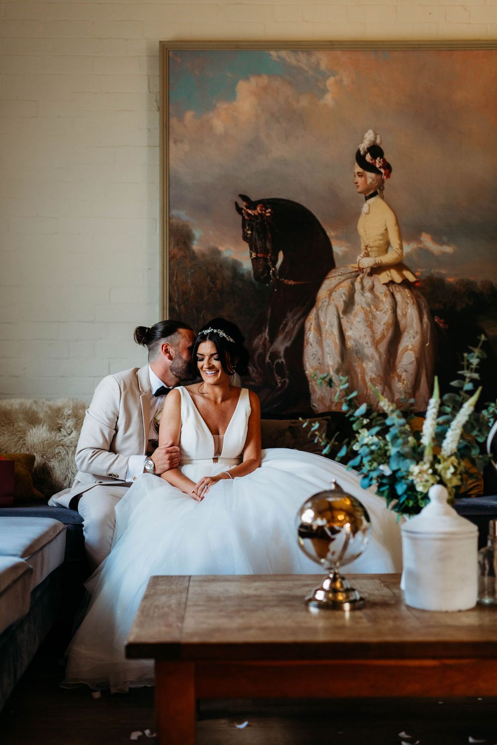 Couple poses in elegant room with vintage equestrian painting and antique globe.