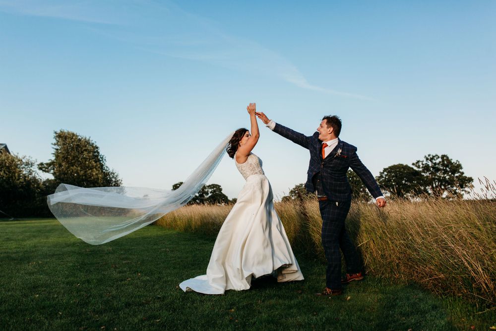 Couple dances in meadow with bride's veil flowing in the wind.