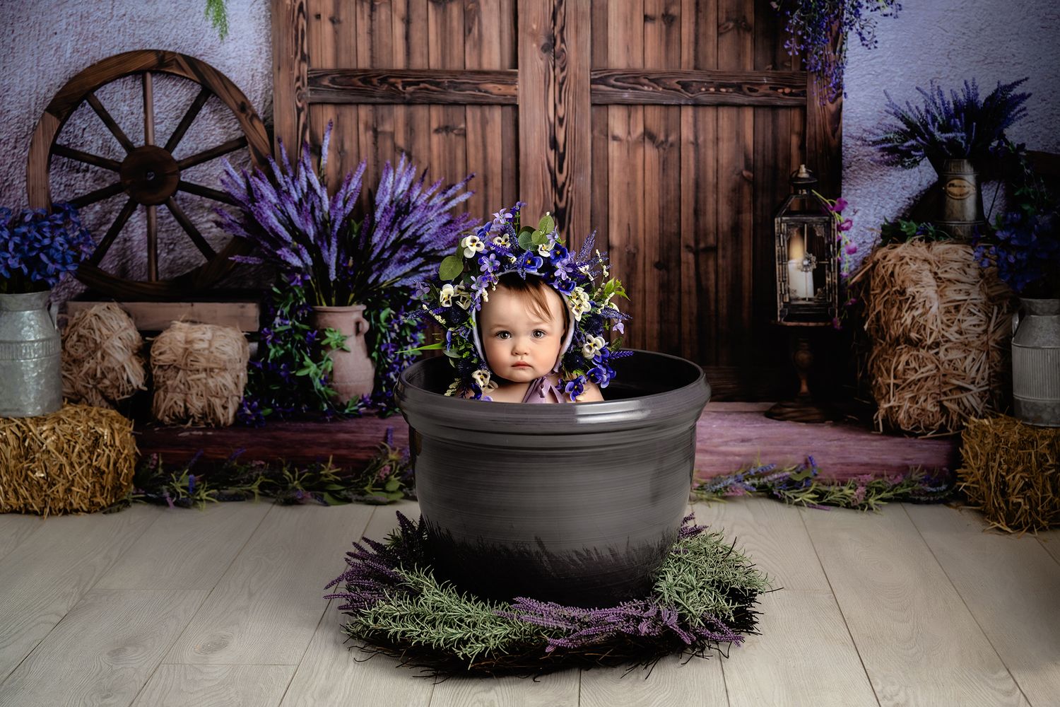 A rustic photography setup with a large gray planter pot surrounded by hay bales and decorative purple flowers.