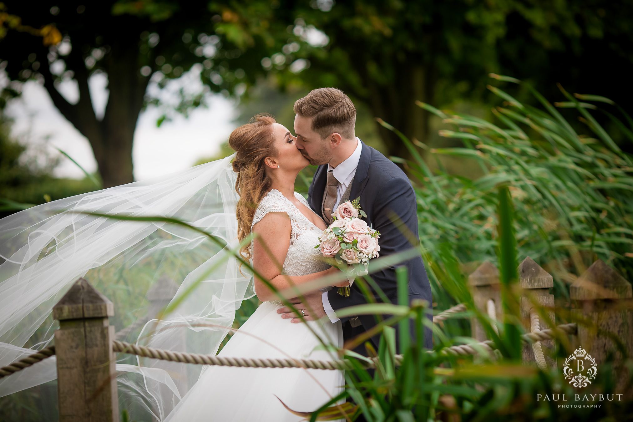 A romantic wedding portrait with tall grasses framing the couple as the bride's veil flows in the breeze.