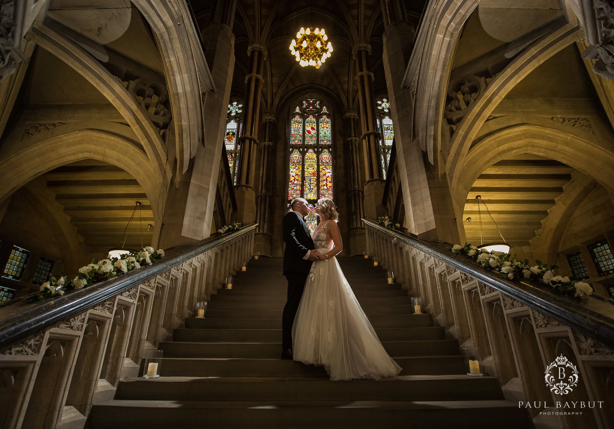 A couple stands on grand cathedral stairs with ornate Gothic architecture and stained glass.