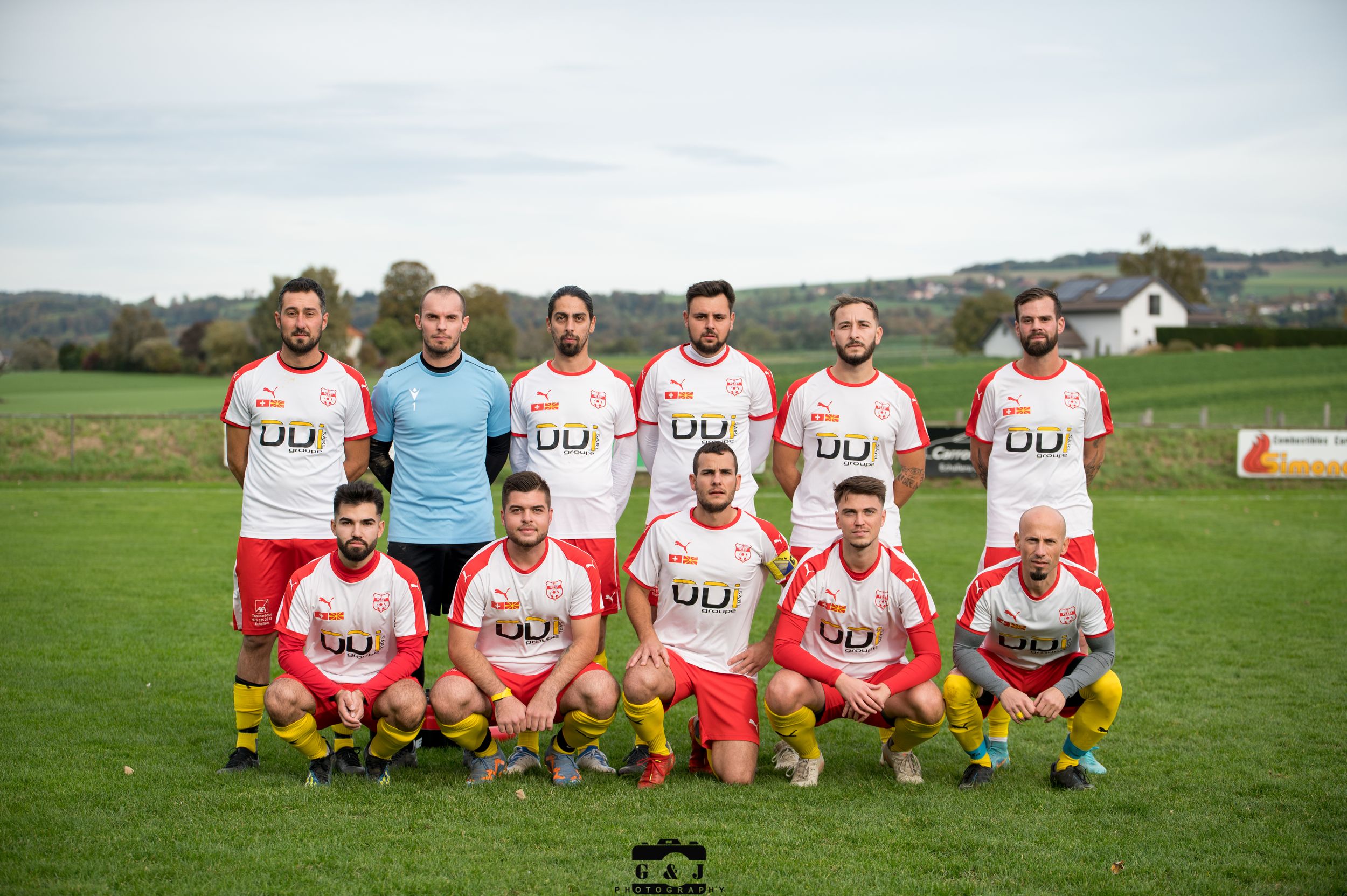 Soccer team players sitting in a row on grass field for team photo.