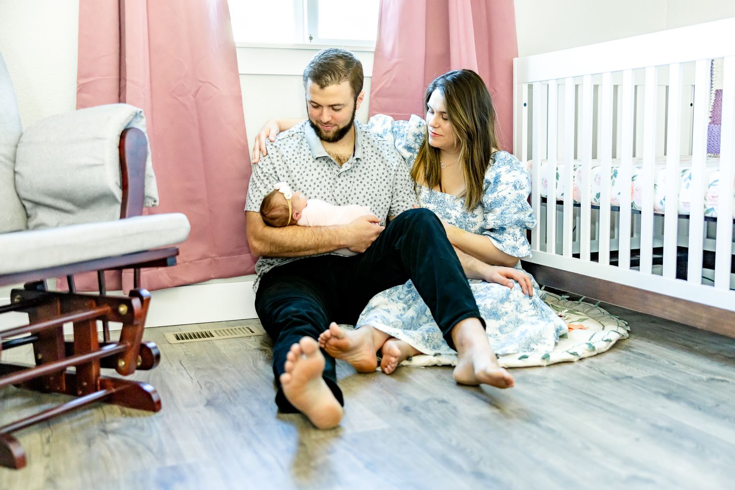 Parents sit together on floor gazing at baby girl in dad's arms during newborn photos in Colorado Springs.