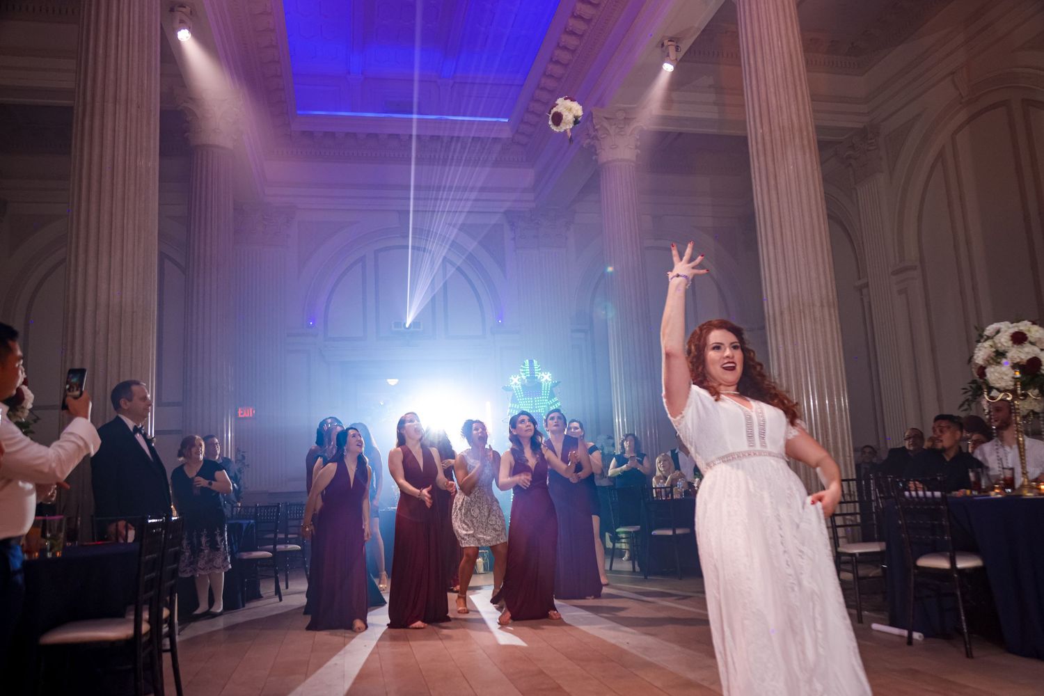 A joyful celebration on a dance floor with bright blue lighting illuminates an elegant venue with classical white columns.