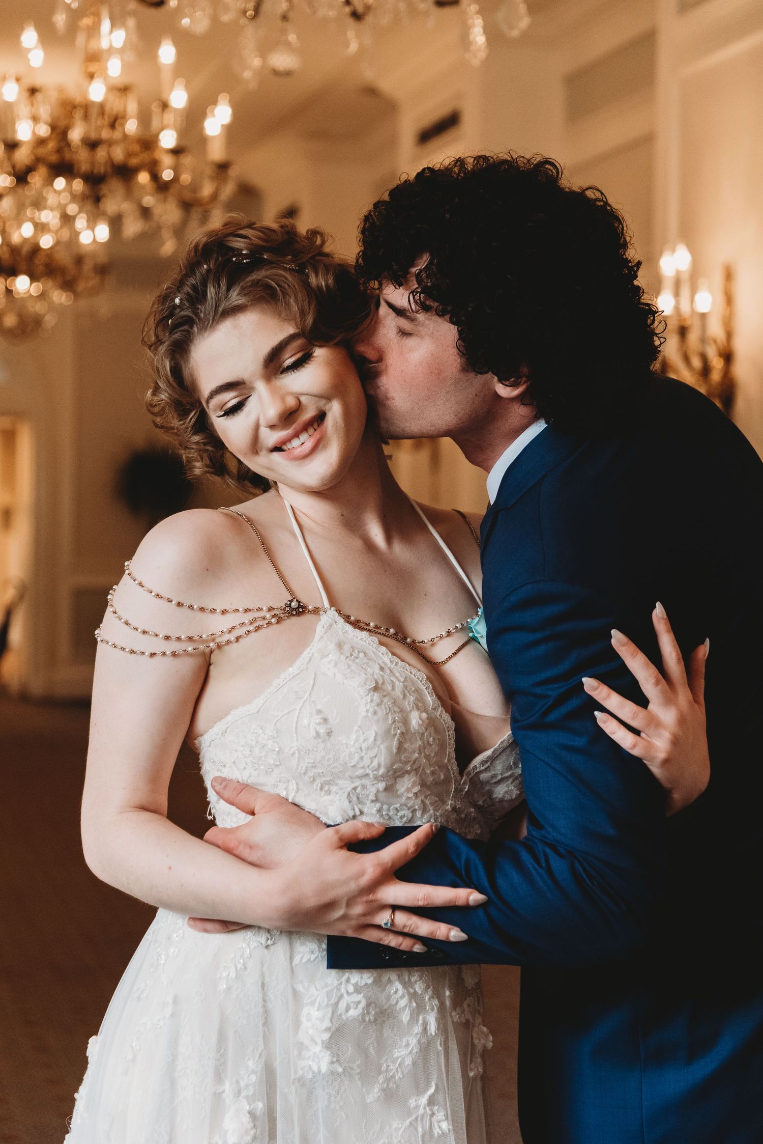 Elegant couple shares romantic moment at formal event with chandeliers in background.