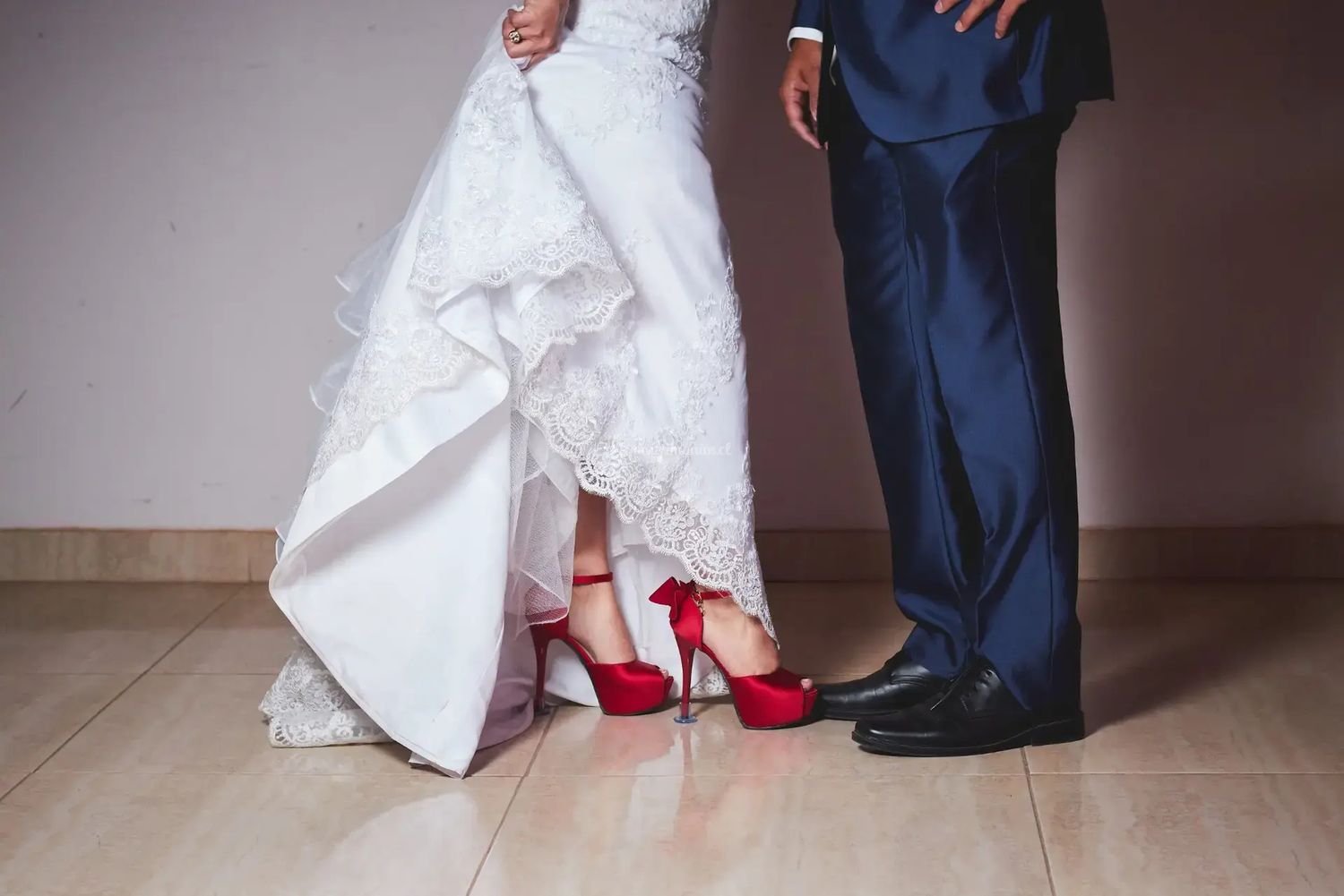 Wedding detail shot showing bride's red shoes next to groom's black shoes on wooden floor.