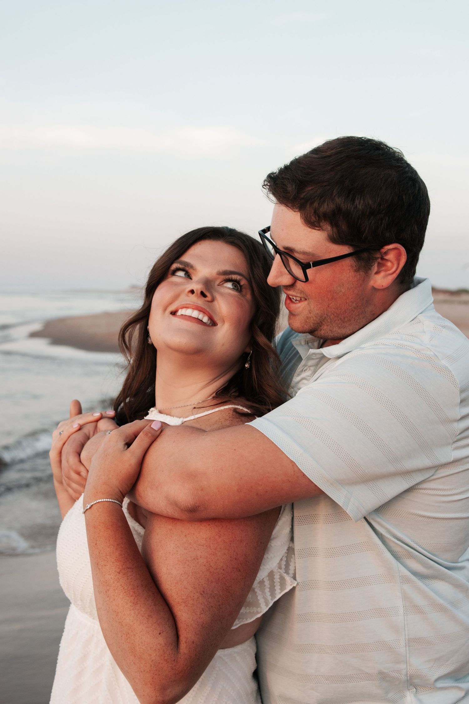 A loving couple embraces on the beach during sunset.