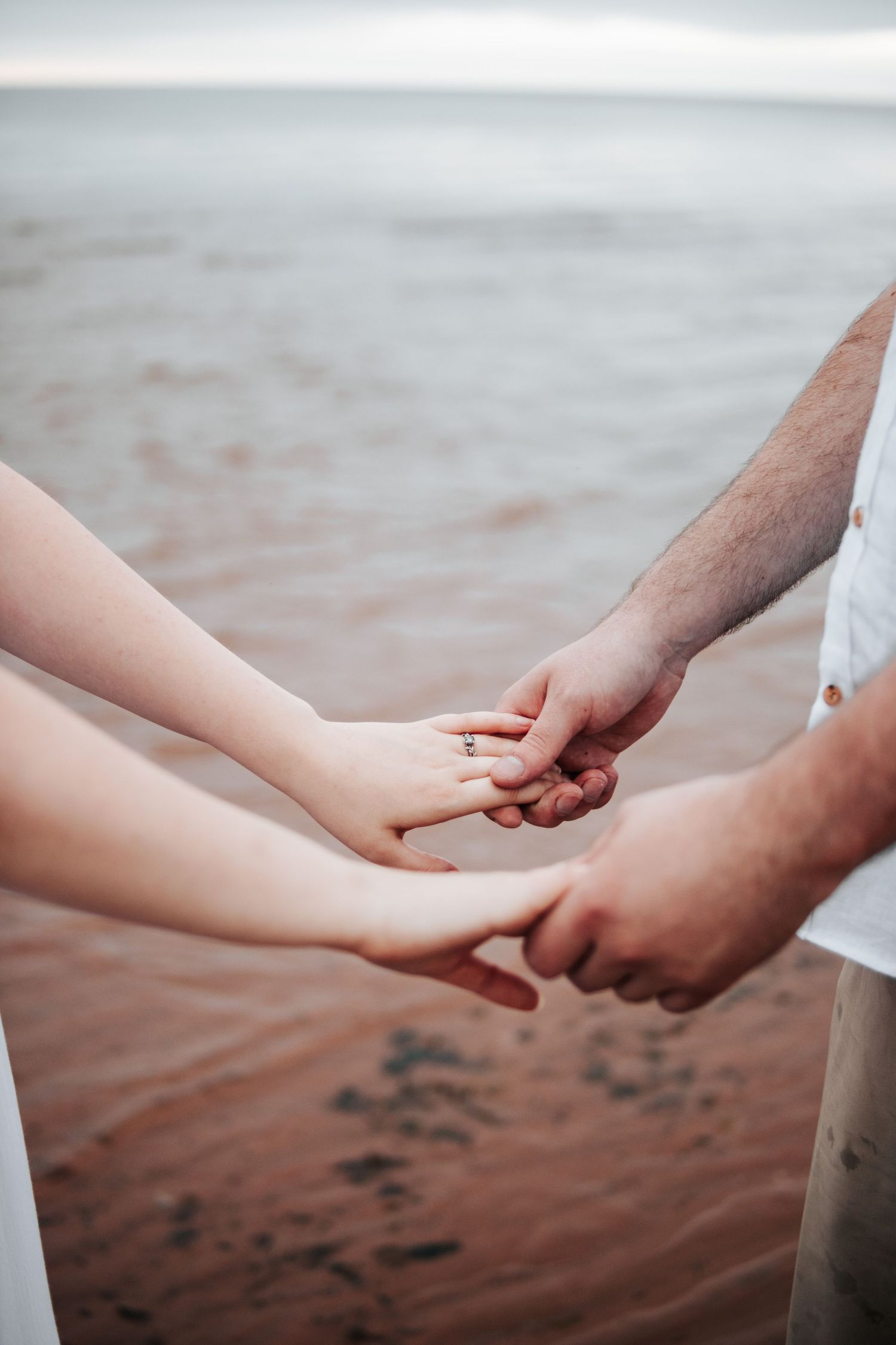 Close-up of two hands tenderly holding each other against a beach backdrop.