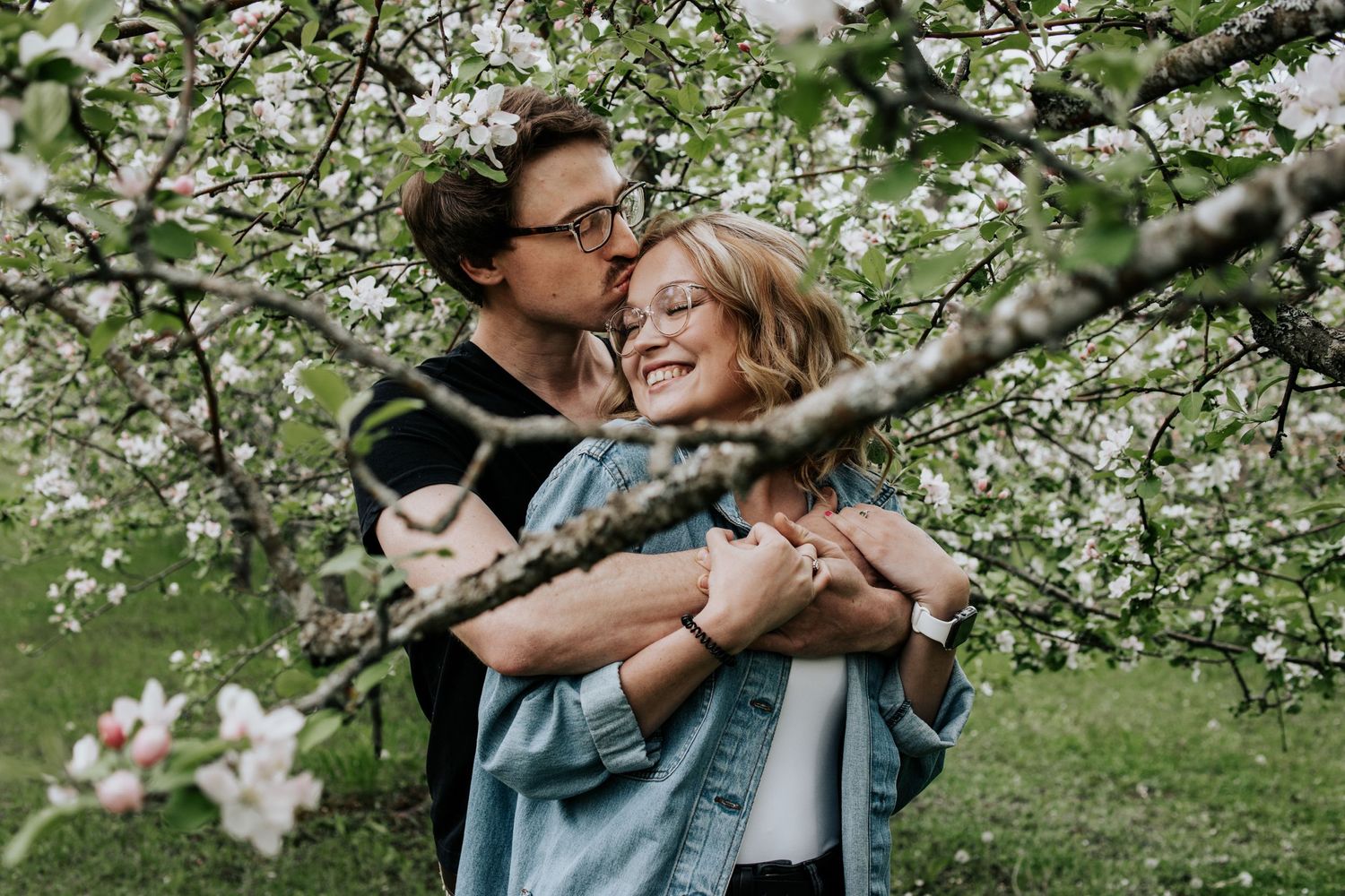 Couple sharing an intimate moment among blooming cherry blossom trees.