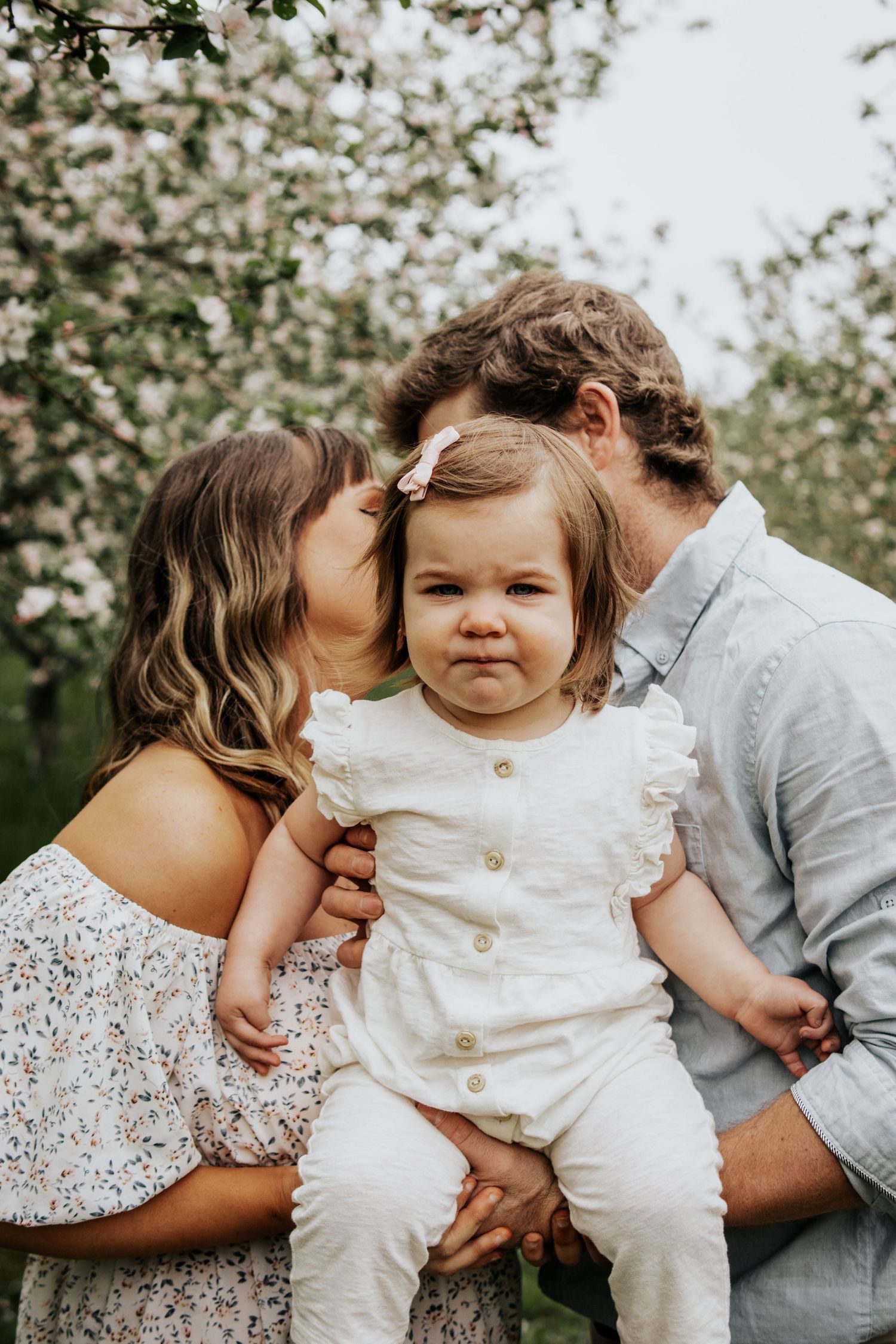 Family portrait under blooming spring trees with a small child in white.