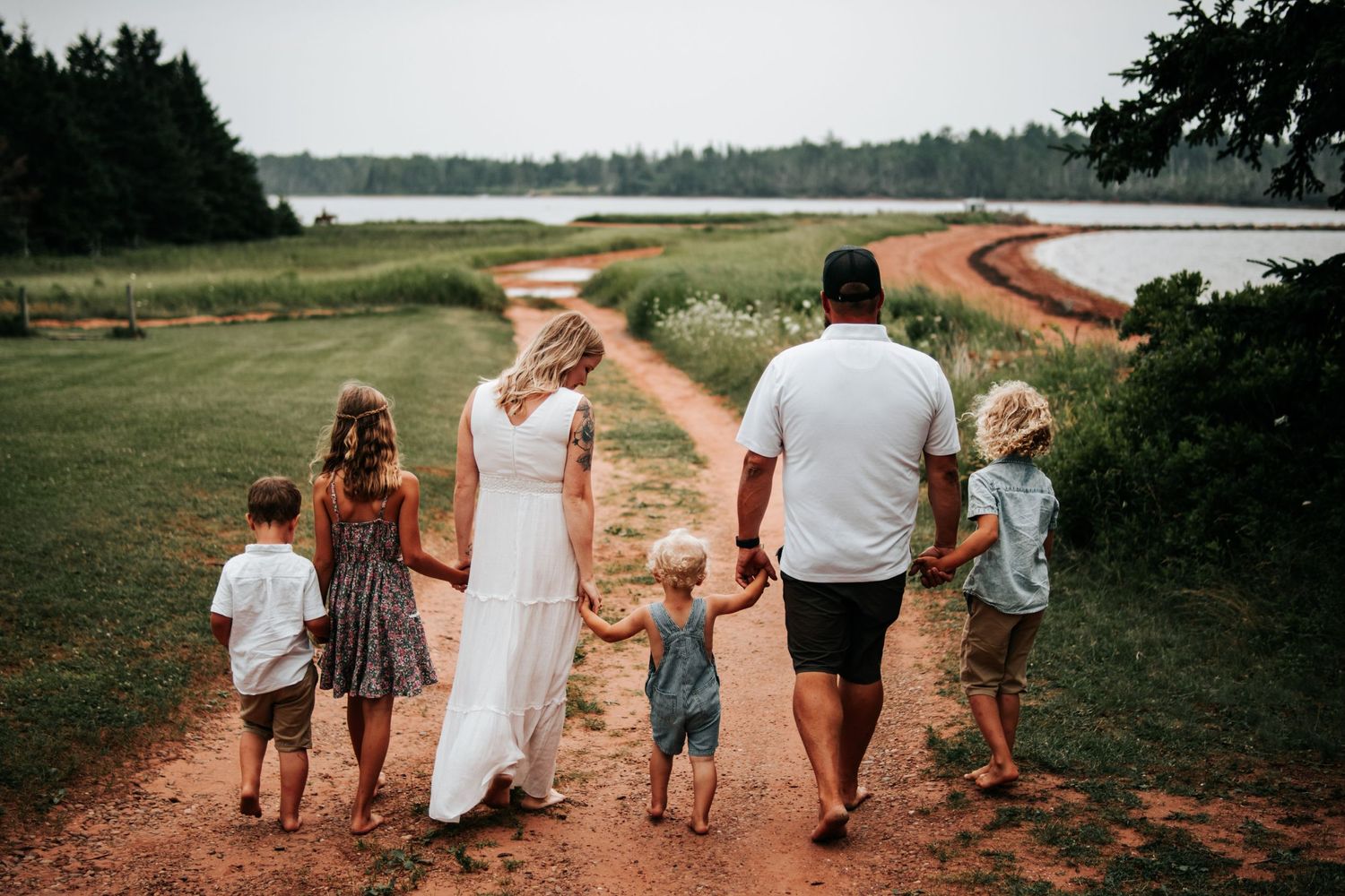 A family walks together along a winding dirt path beside a lake during a summer afternoon.