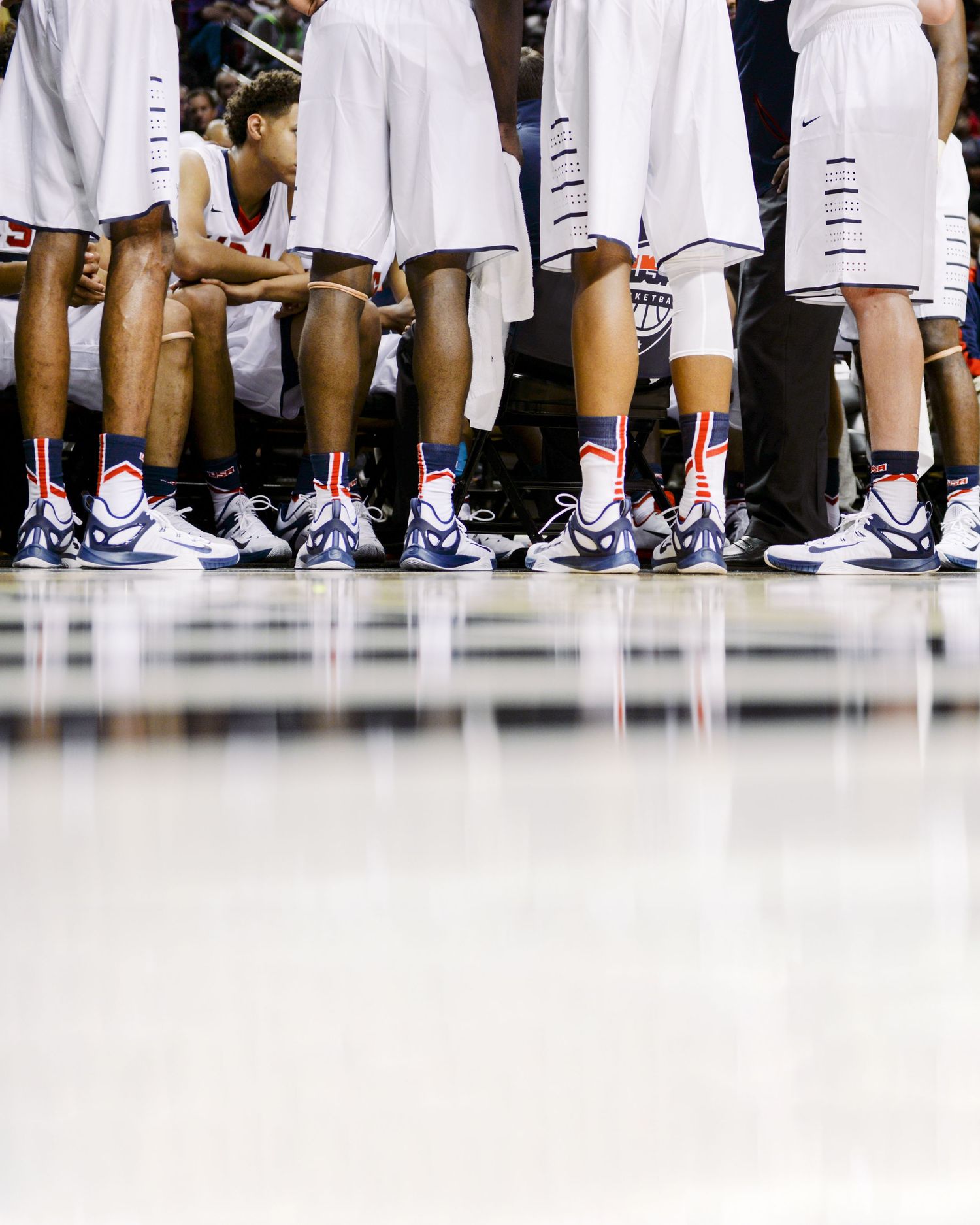 Row of basketball players' legs and sneakers lined up on court during game.