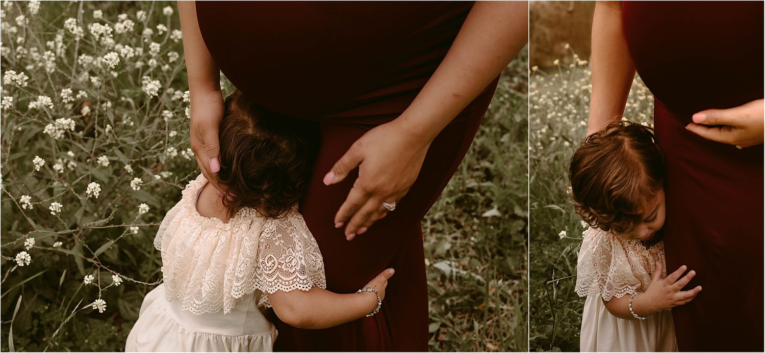 Mother in burgundy dress and child in cream dress share intimate moment among wildflowers.