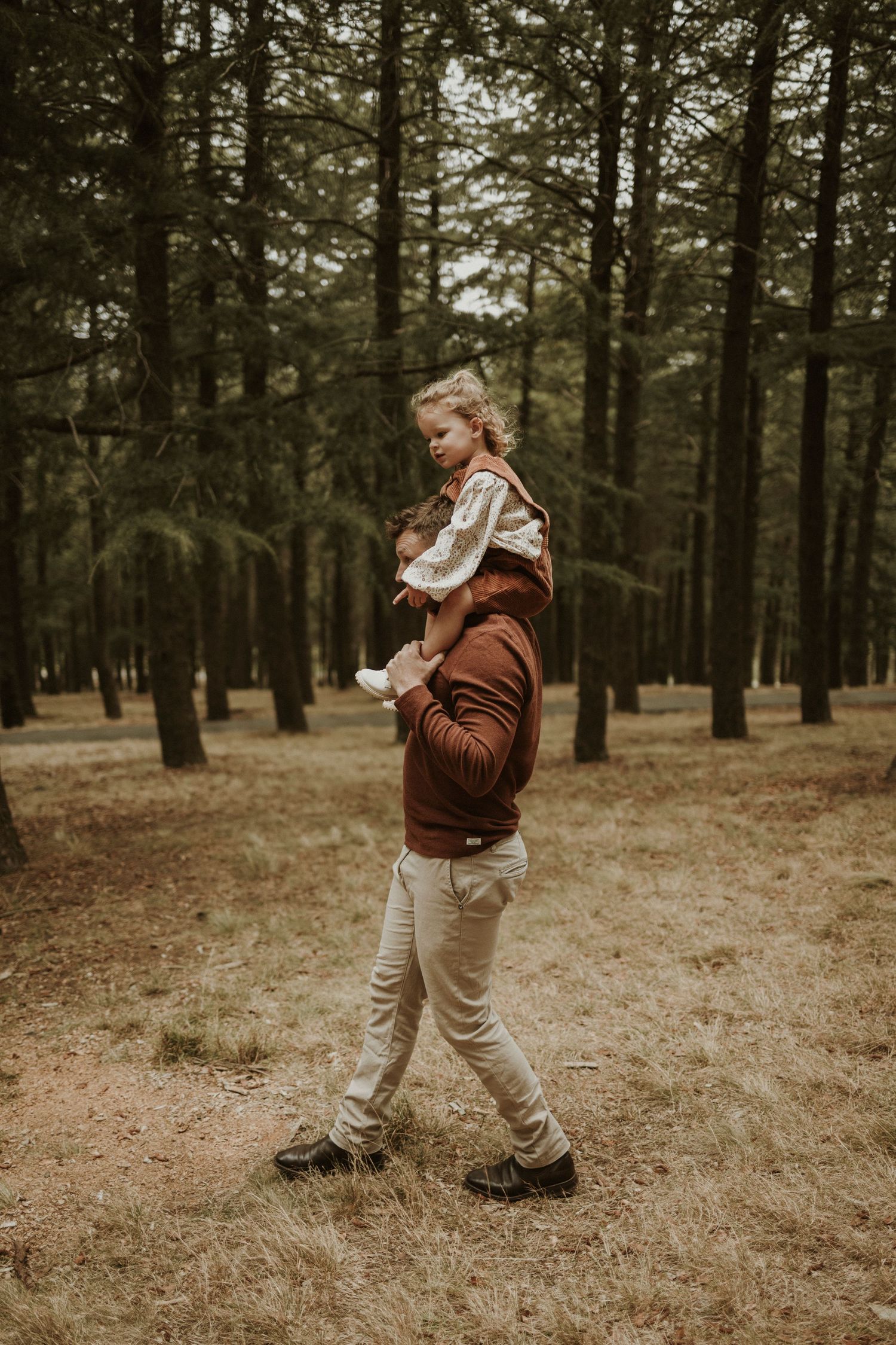 Daughter on fathers shoulders as they walk through the forest