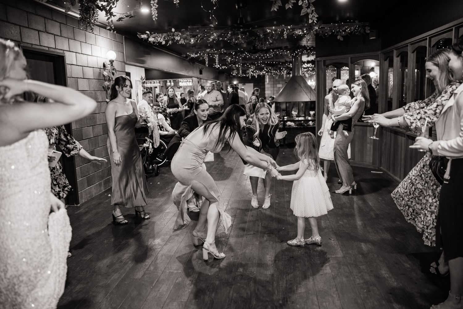 Black and white photo of wedding guests dancing on indoor dance floor with festive energy.