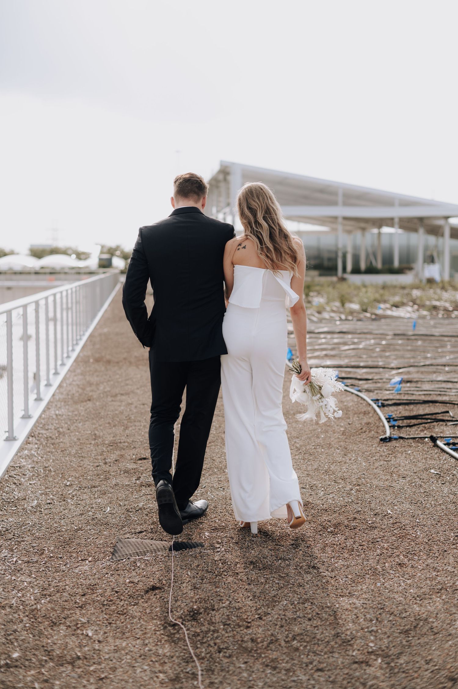 Wedding couple walking along path with modern structure in background.
