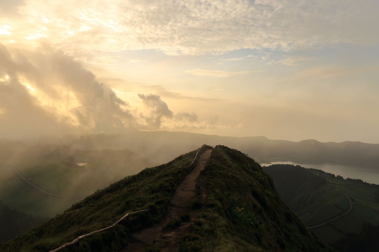 Narrow dirt path traversing a dramatic mountain ridge during golden hour.