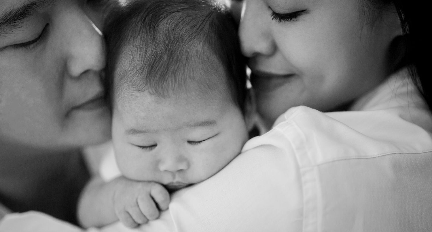 mum and dad giving sleeping baby a kiss
