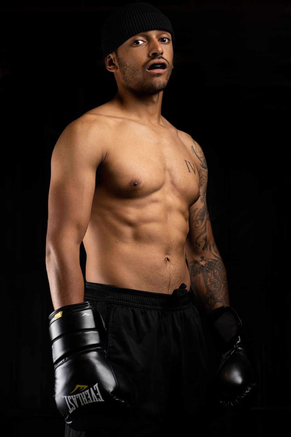 Athletic boxer in beanie and gloves poses against dark background.