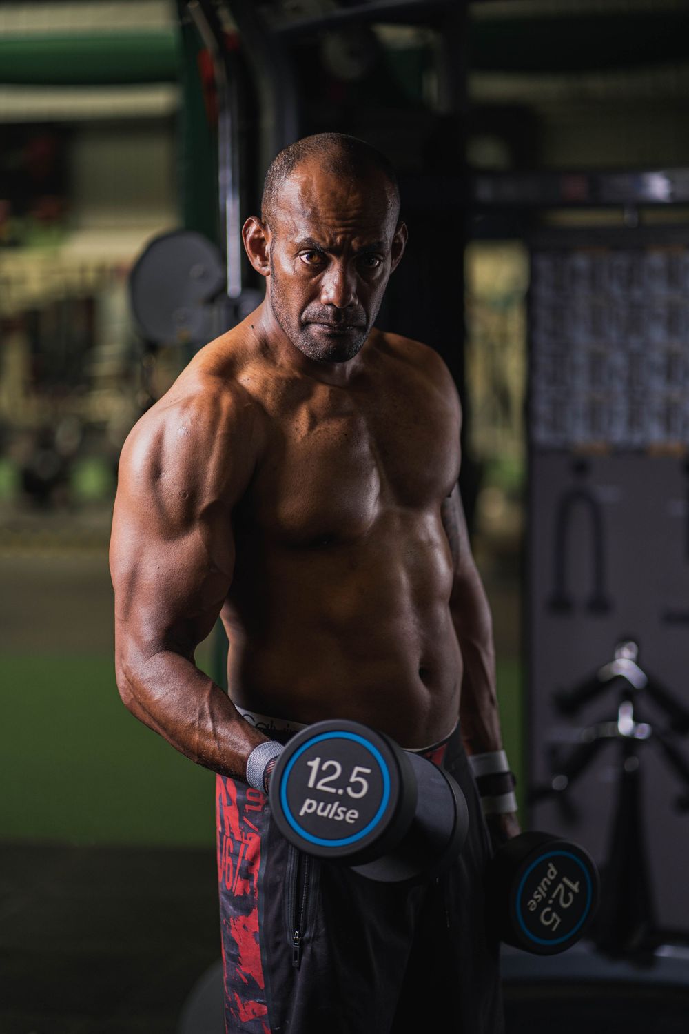 Muscular person exercising with dumbbells in a dimly lit gym environment.