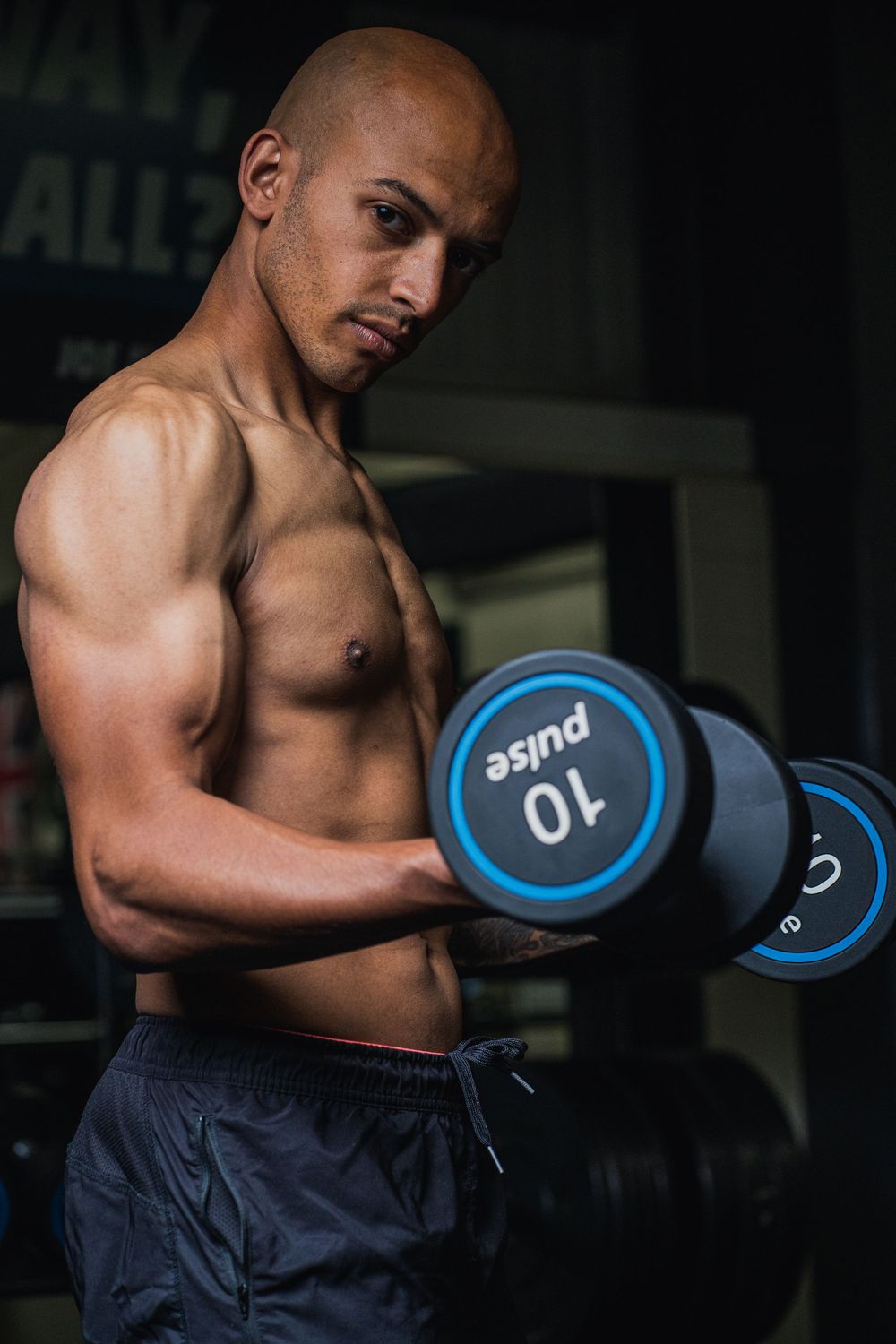 Athletic person lifting blue dumbbells during workout session in dark gym setting.