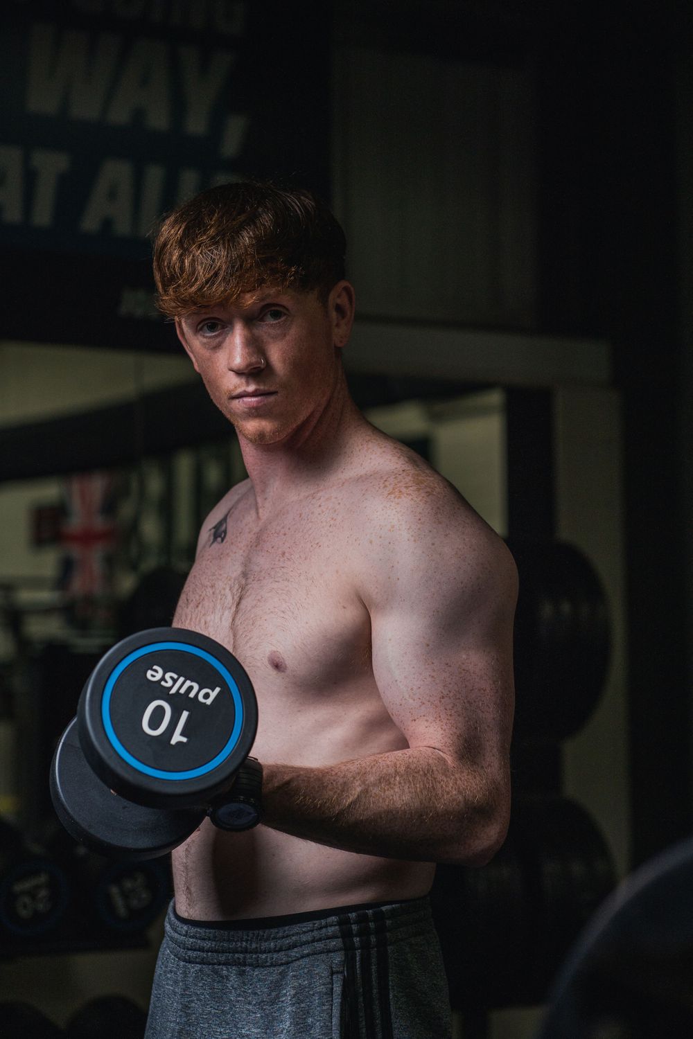 Person performing dumbbell exercise in moody gym lighting with determined expression.