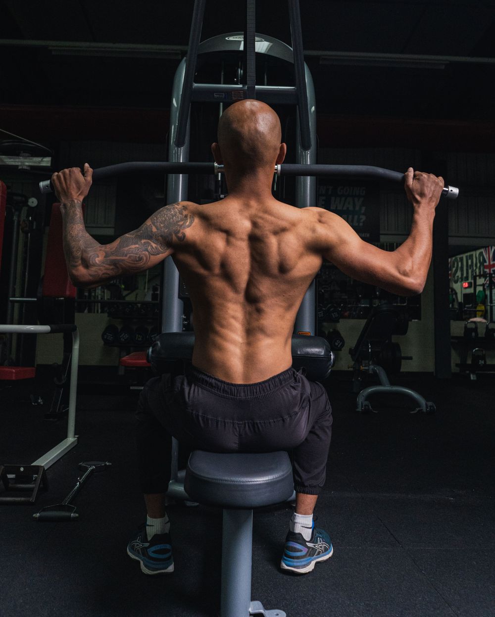 Shirtless person with tattoos performing lat pulldown exercise showing defined back muscles.