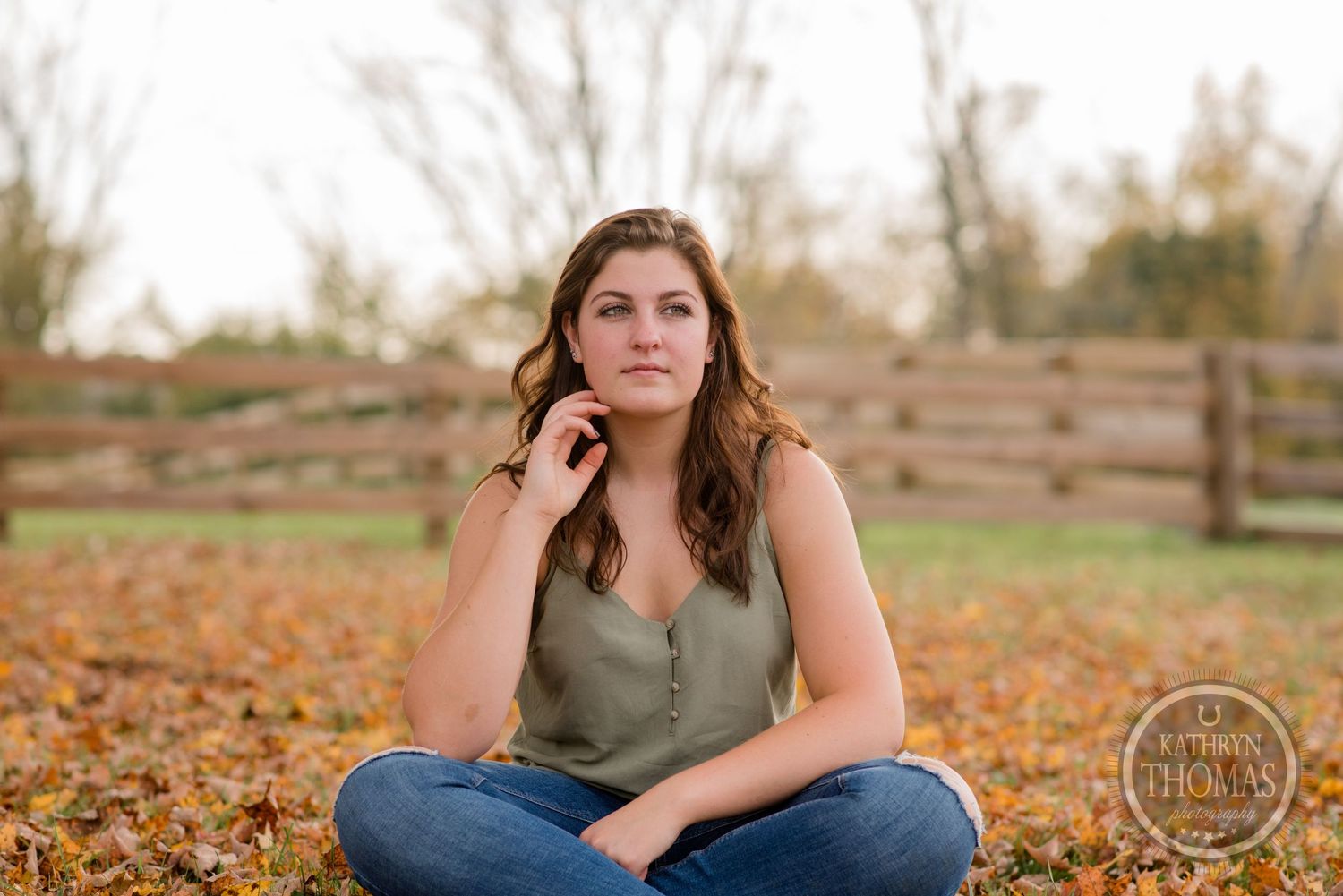 Casual outdoor portrait in a rustic fall setting with wooden fence and autumn foliage.