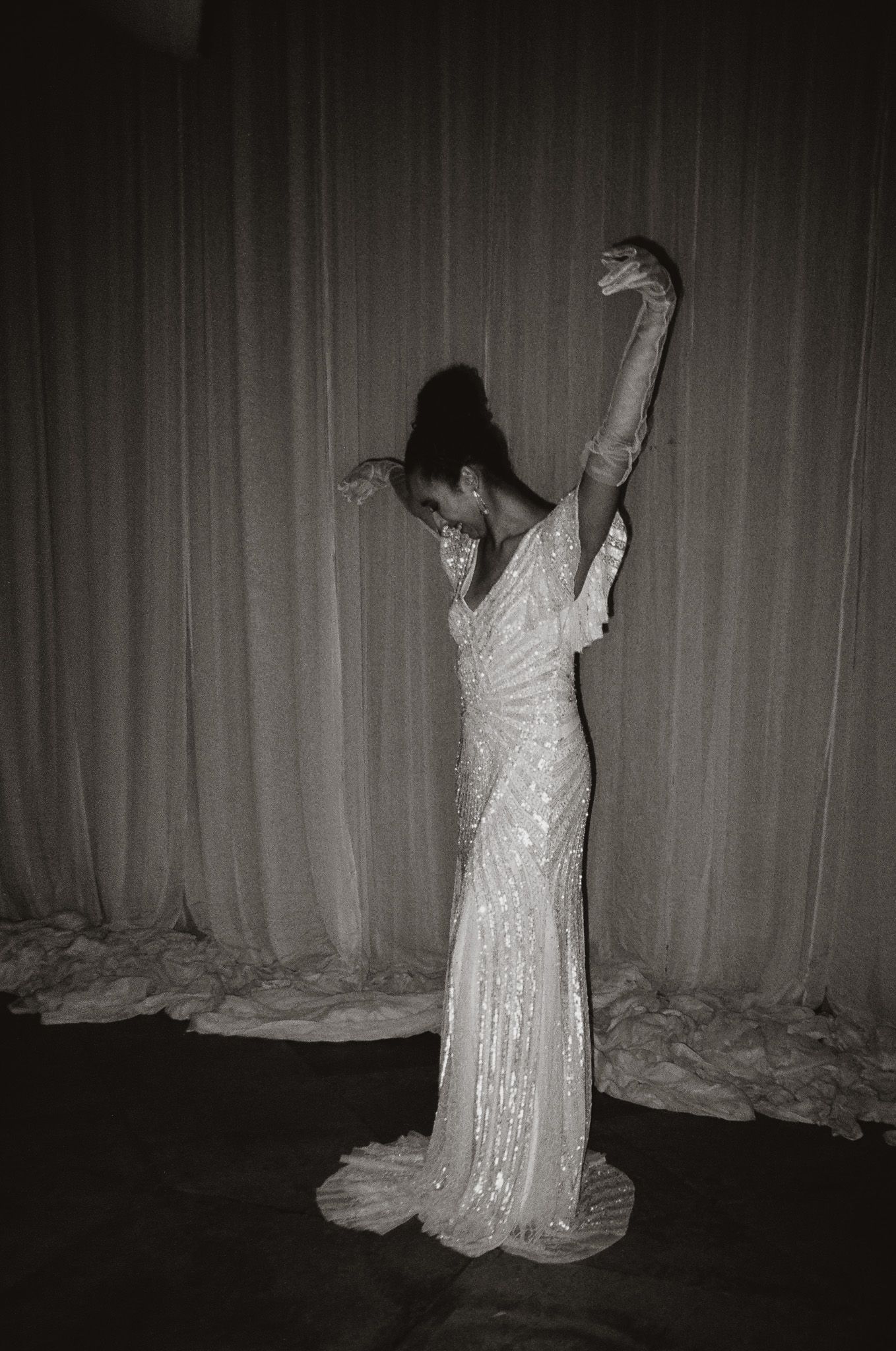 Silhouette of person in sequined dress posing dramatically against curtain backdrop.