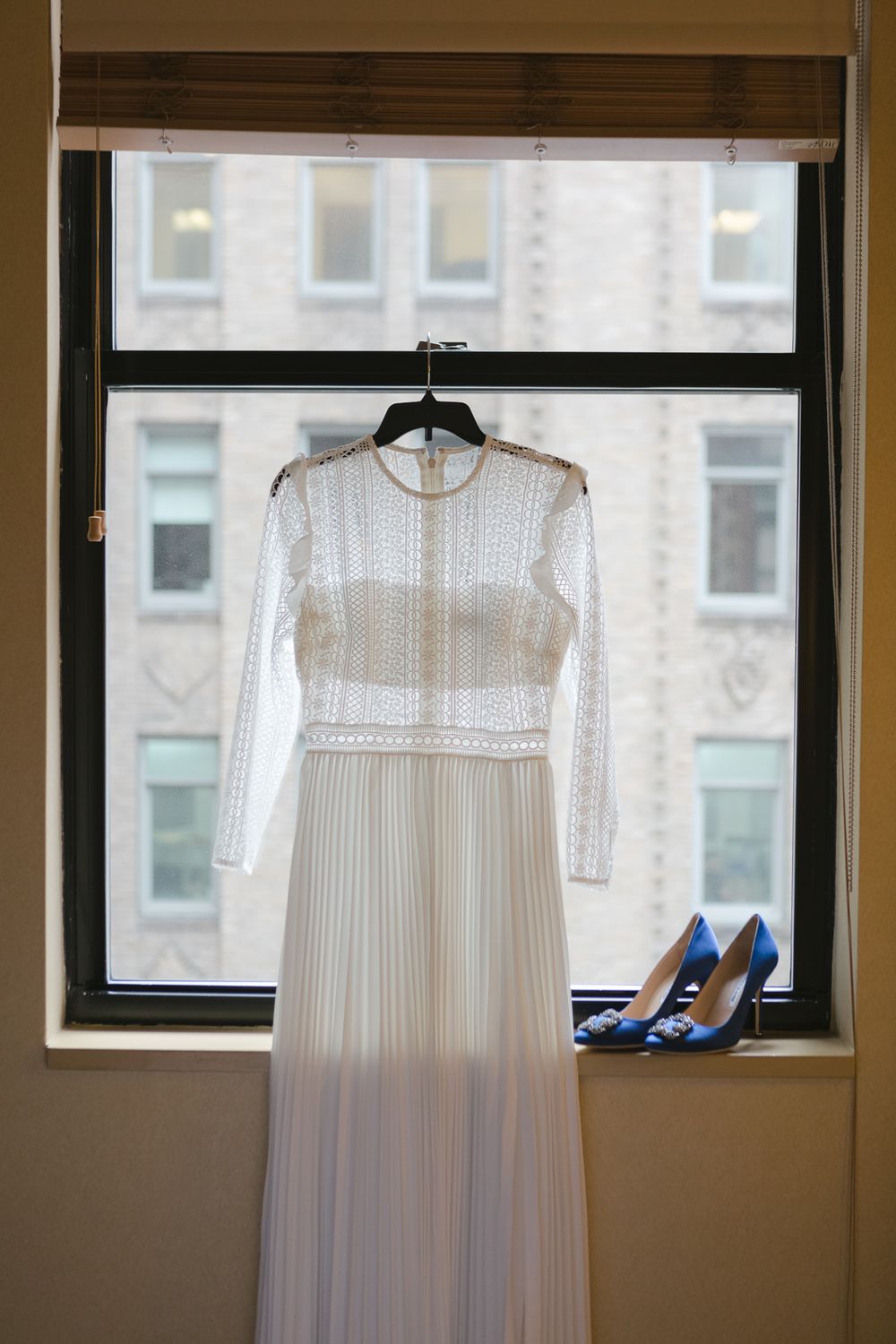 a view of a wedding dress and Jimmy Cho shoes against a window, photo by NYC elopement photographer Paula Ortiz