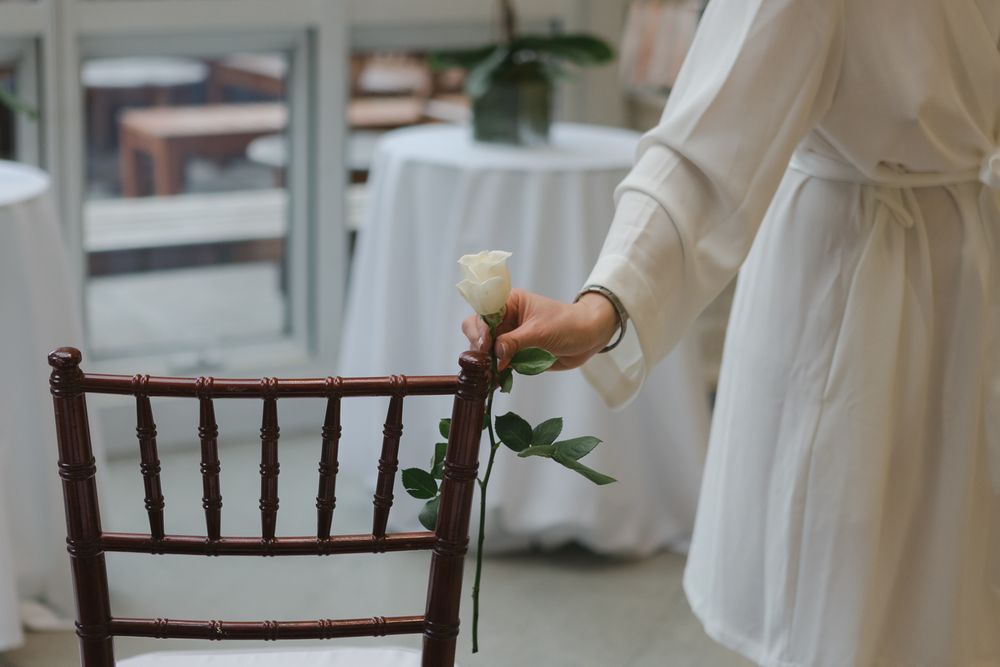 a detail view of a woman's hand holding a white rose in wedding ceremony room, photo by NYC elopement Paula Ortiz