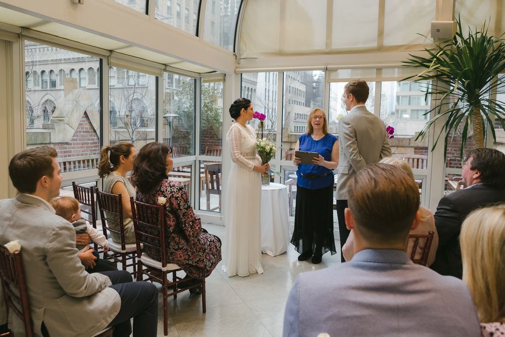 a couple stands in front of the officiant surrounded by sitting family in the rooftop of the Library Hotel in NY