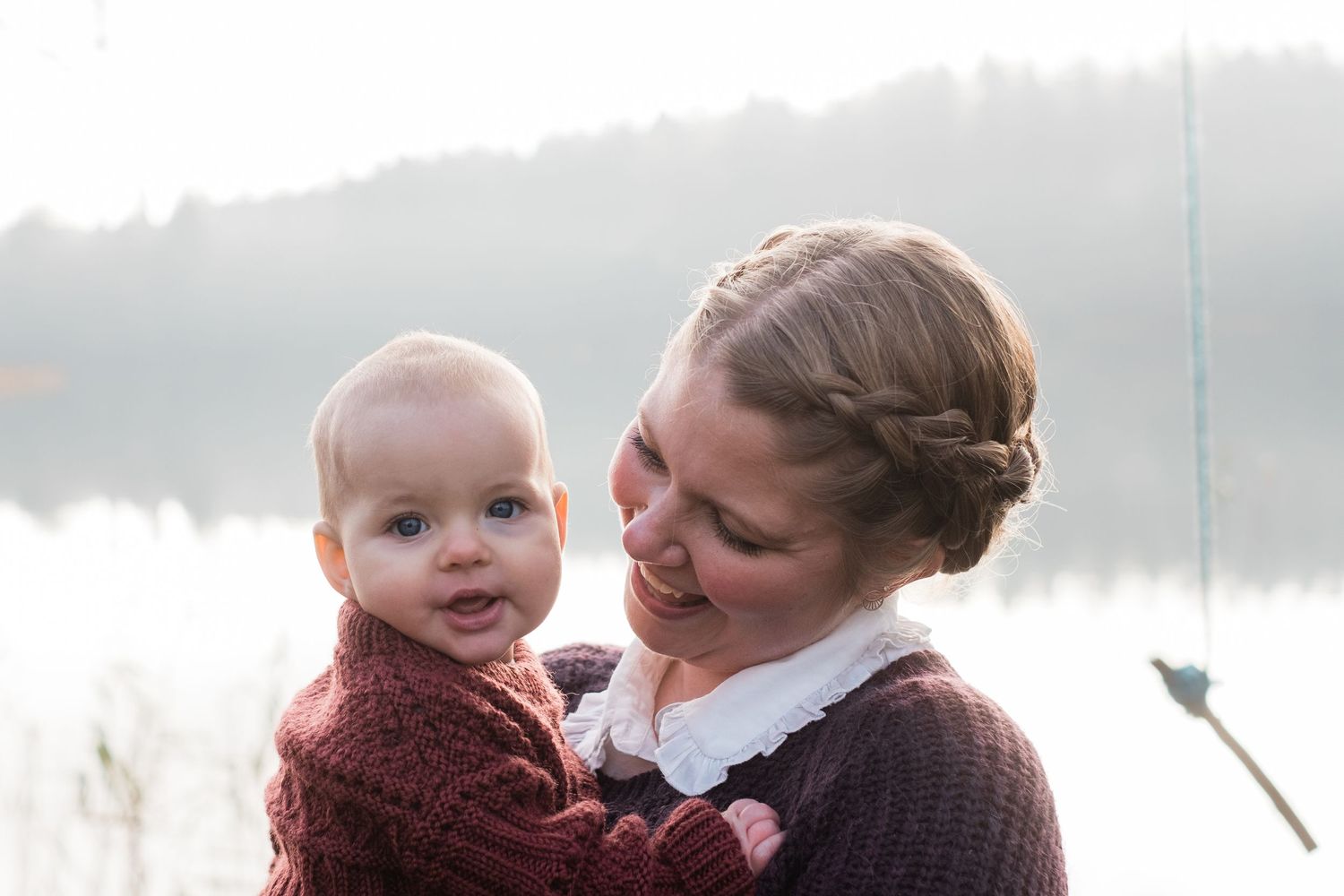 A heartwarming moment between parent and baby against a misty lake backdrop.