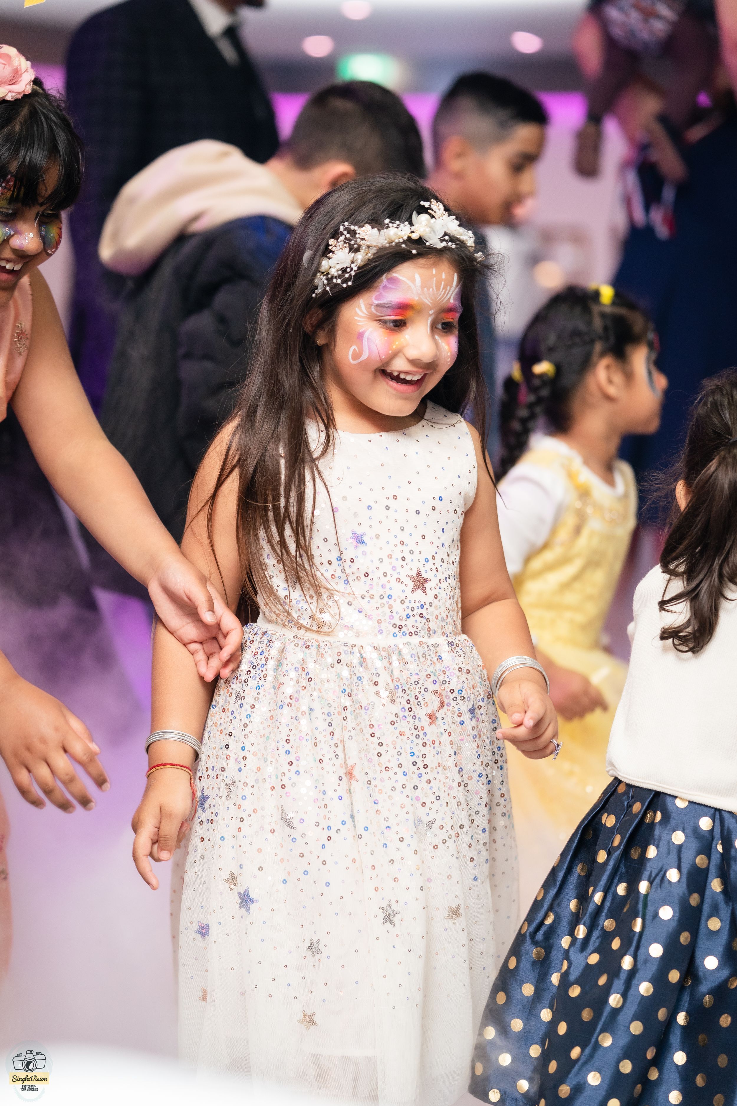 Young girl with face paint and floral crown smiling while dancing at a birthday party celebration.