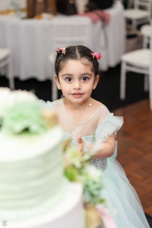 Wide-eyed little girl in mint tulle dress reaching toward her birthday cake at a party celebration.