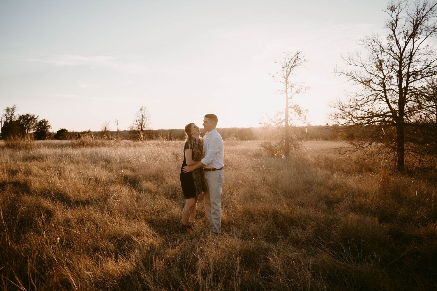 A couple stands together in a field bathed in warm sunset light.