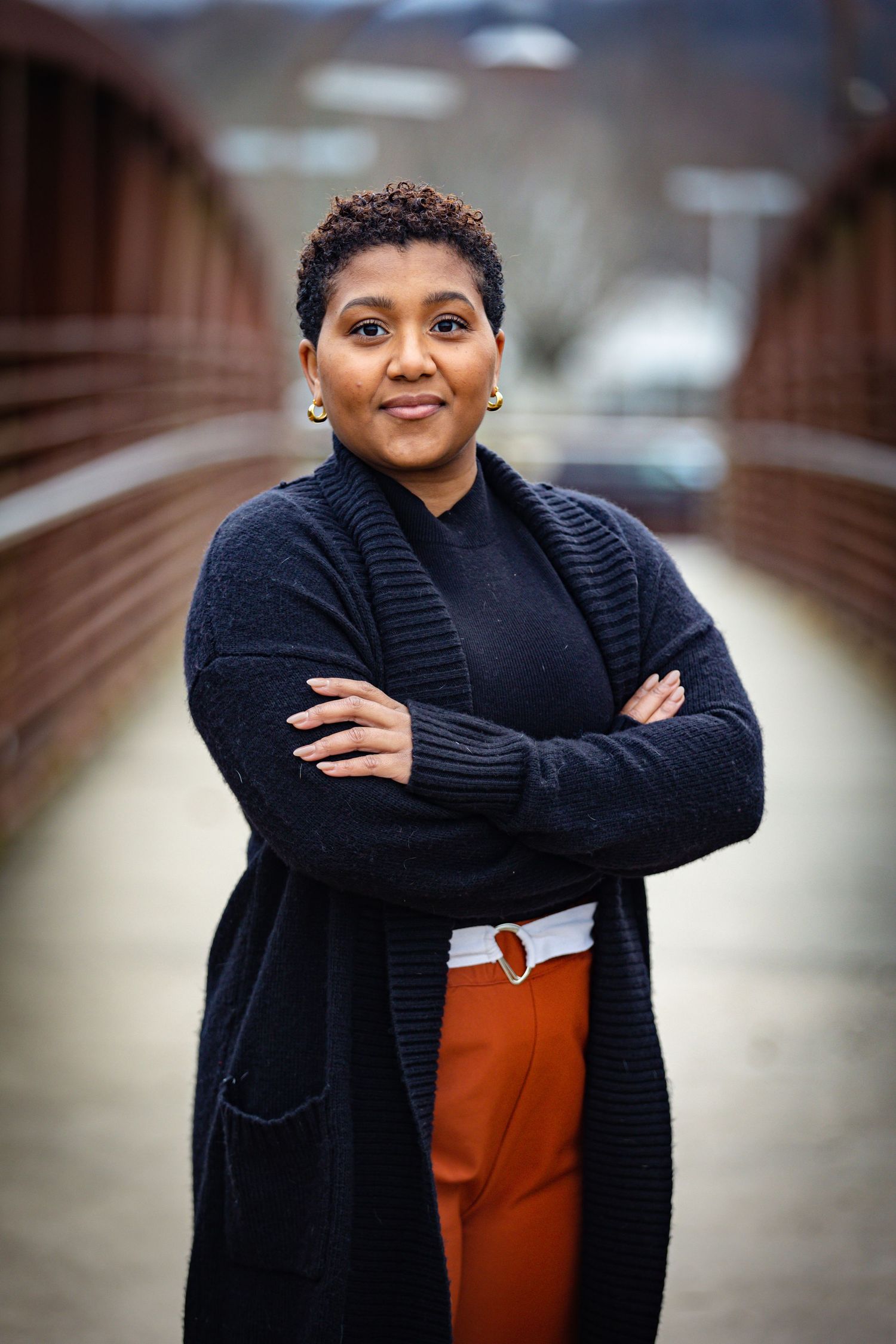 Professional outdoor portrait of person in navy sweater and orange pants on bridge.