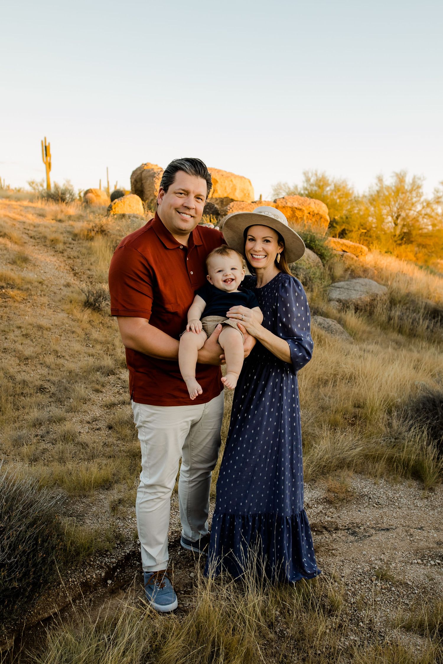 Family of three smiling big in the warm golden glow of the Scottsdale Arizona desert sunset.