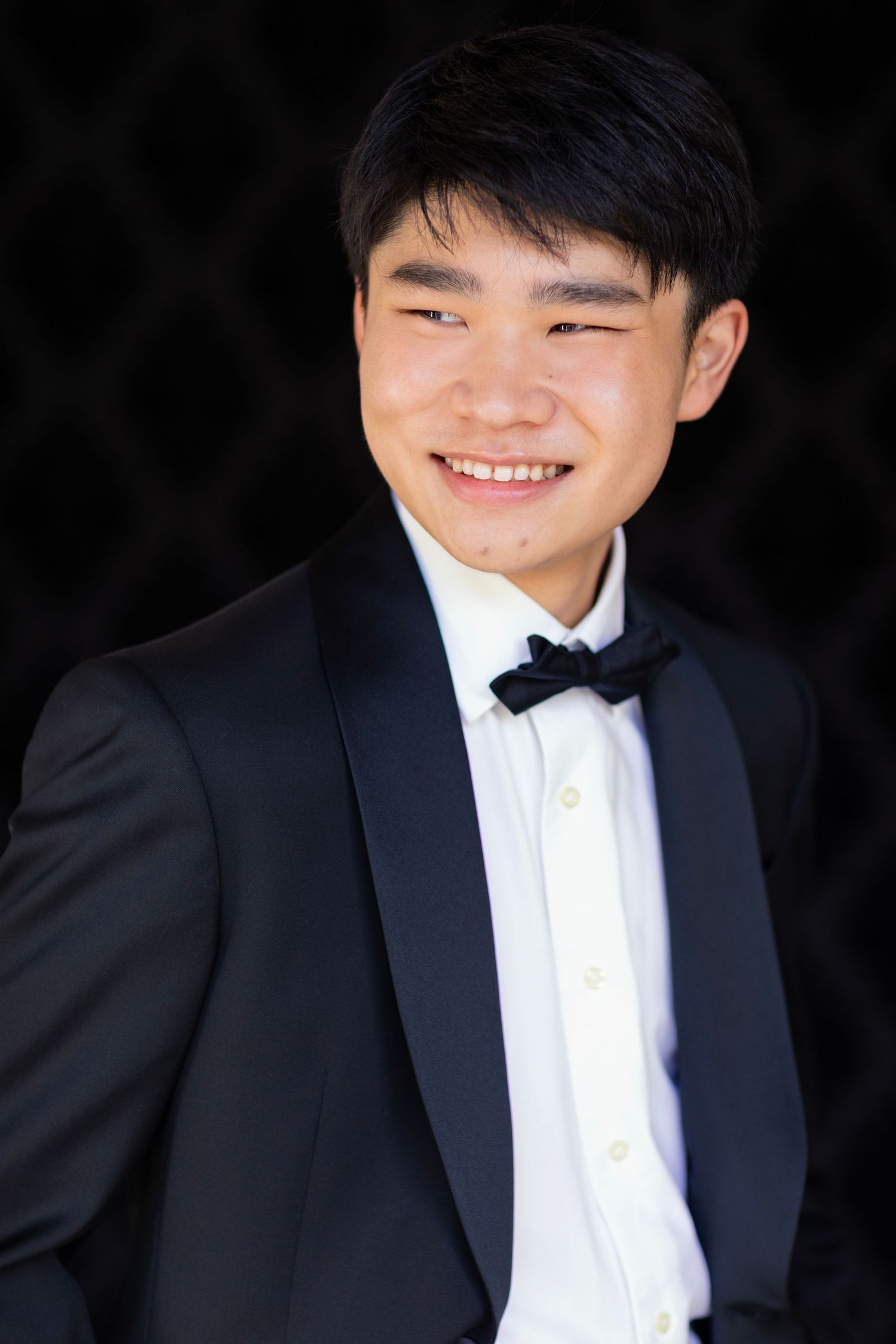 Formal portrait of a high school senior in black tuxedo and bowtie against dark background.