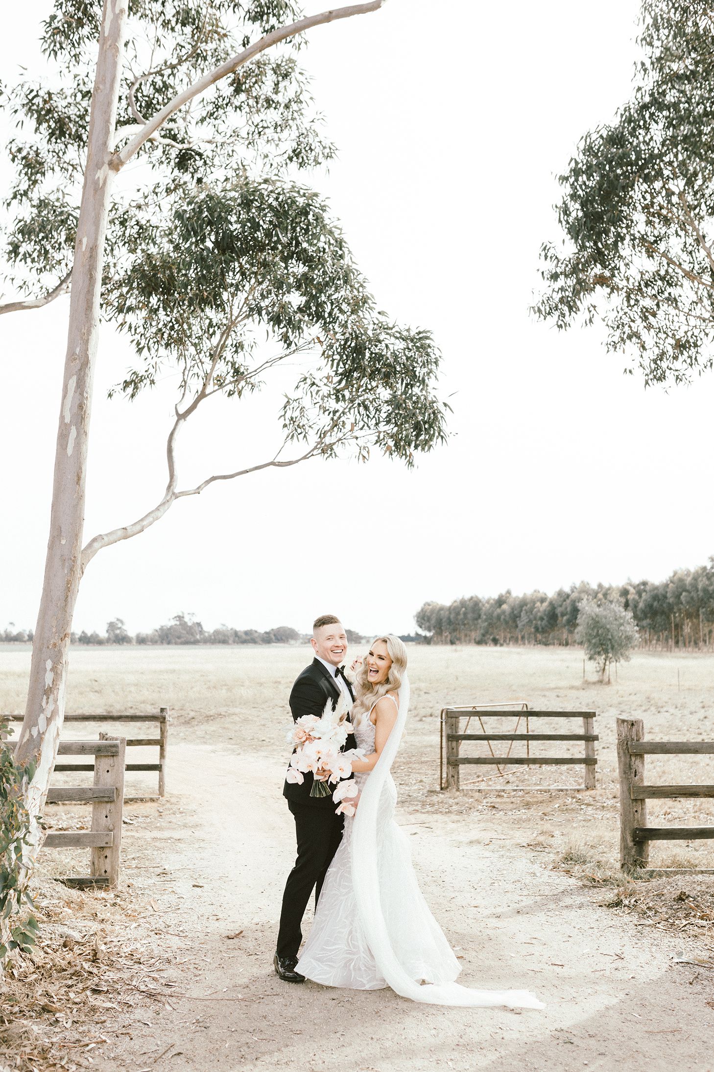Newlyweds posing for photos in a rustic outdoor setting with wooden fence details.
