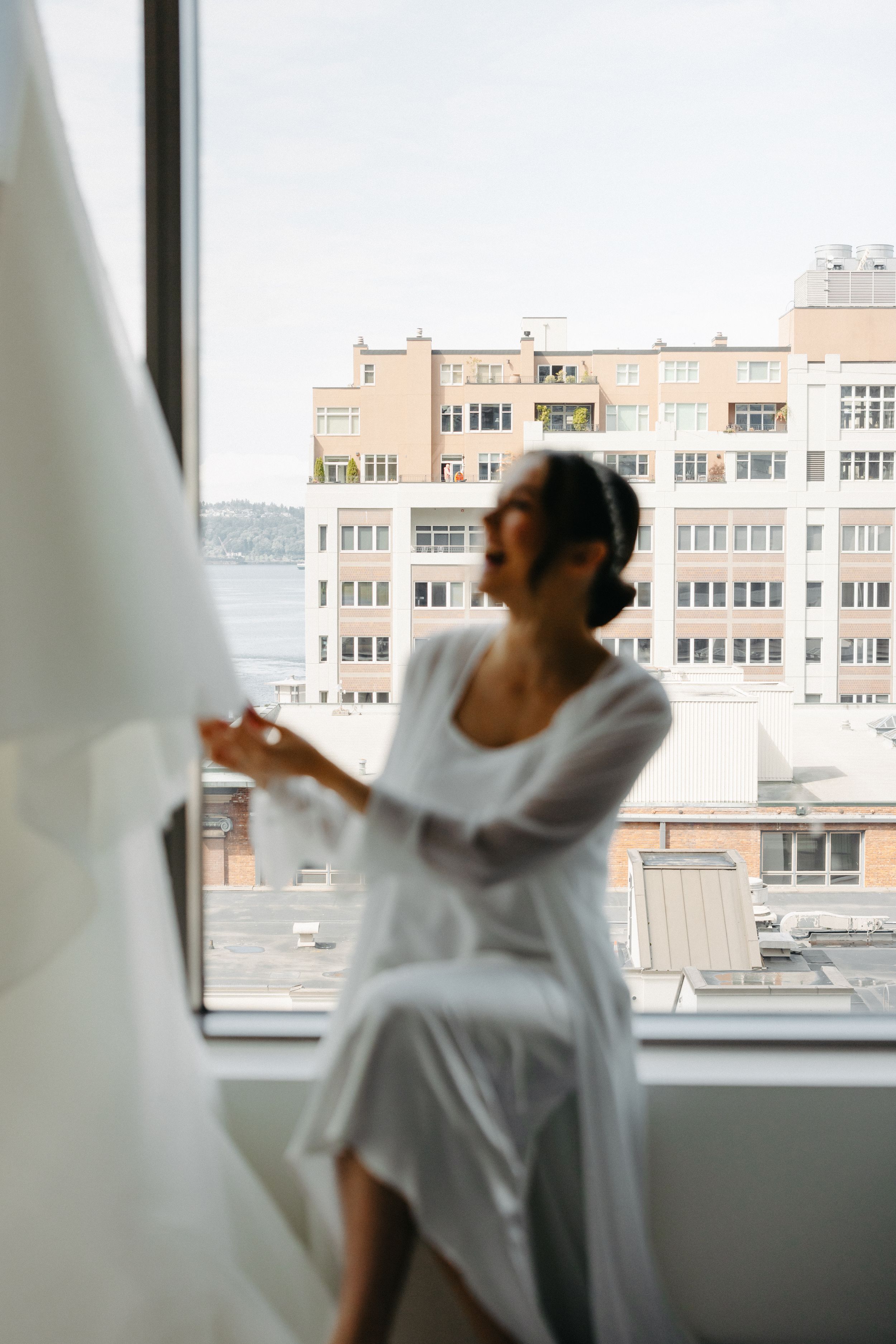 Silhouette of person in white robe against city window during wedding preparations.