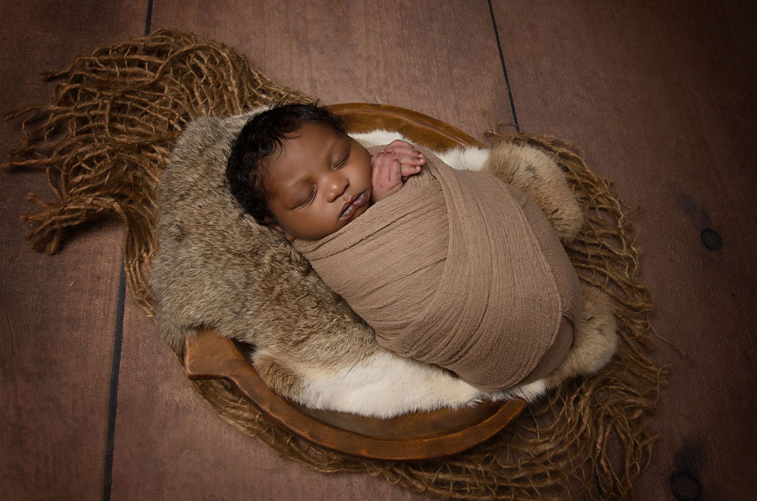 Sleeping swaddled newborn lying in wooden bowl with rustic textured background.