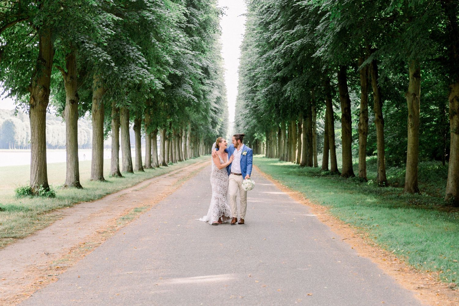 A married couple walking through the tree lined path at Versailles.