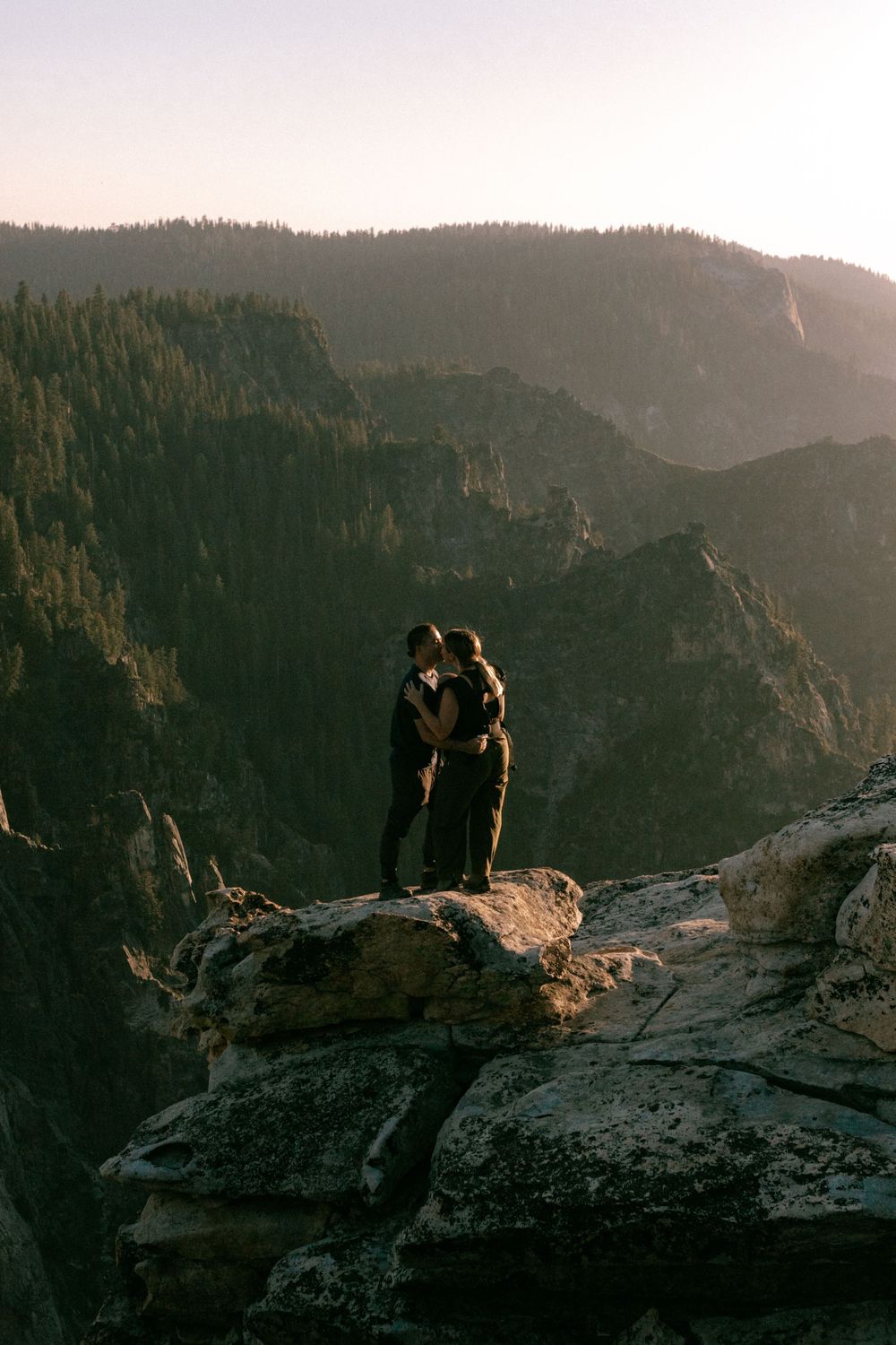 A silhouetted couple stands together at sunset overlooking a dramatic mountain canyon landscape.
